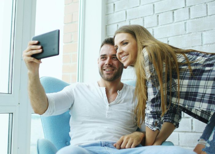 Happy Couple Sitting Together At Home And Smiling For A Selfie On A Tablet.