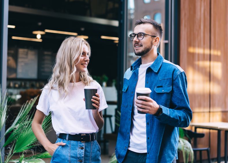 Couple Holding Coffee And Talking Outside A Café