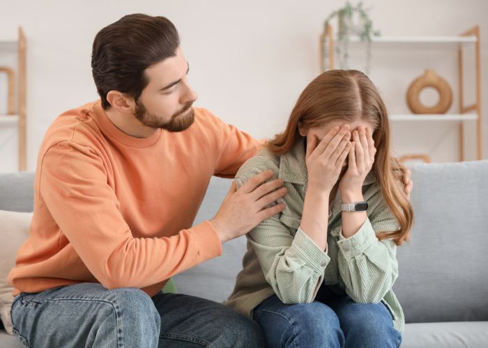 Man Comforting A Crying Woman As They Sit Together On A Sofa.