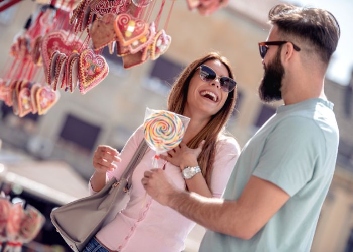 Laughing Couple Shopping Outdoors While Holding A Colorful Lollipop.