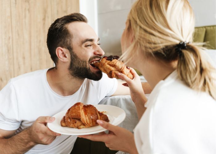 Smiling Couple Sharing Croissants During A Relaxed Breakfast At Home
