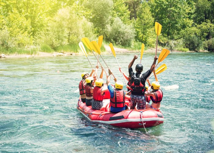 Rafting Group Raises Yellow Paddles While Floating Down A Calm, Tree Lined River.