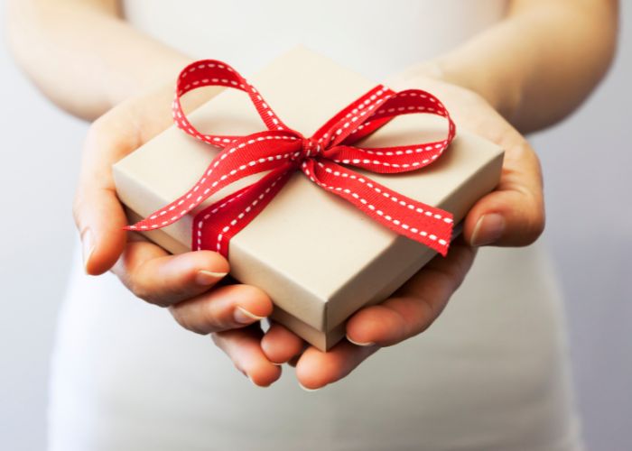 Close Up Of Hands Holding A Wrapped Gift Box With A Red Ribbon