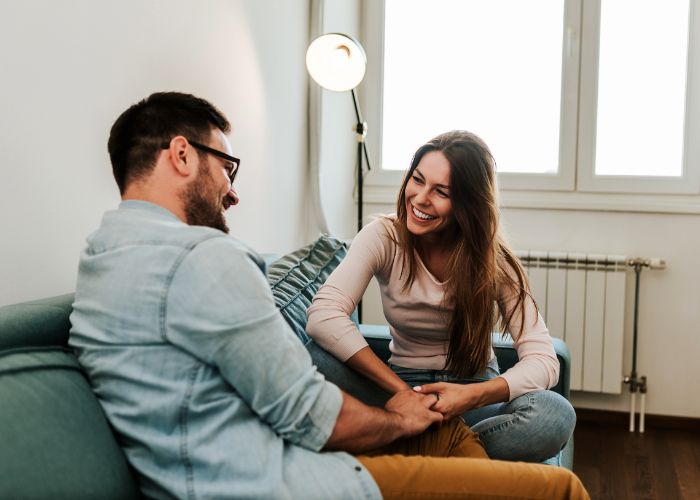 Couple Smiling And Holding Hands On A Sofa During A Warm Conversation