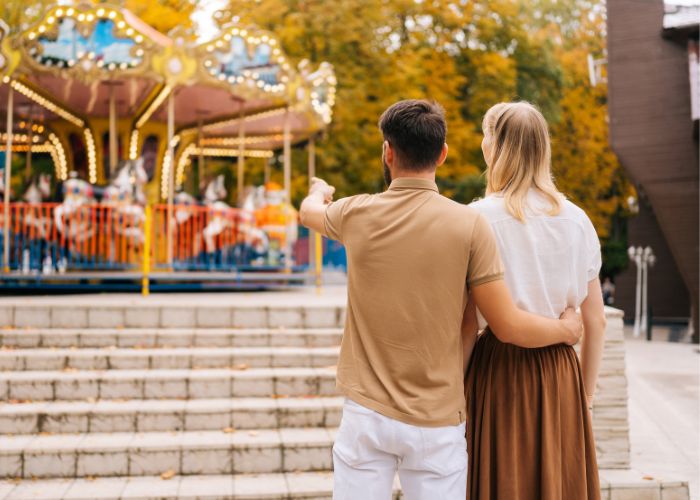 Couple Walking Together Near A Carousel At A Theme Park