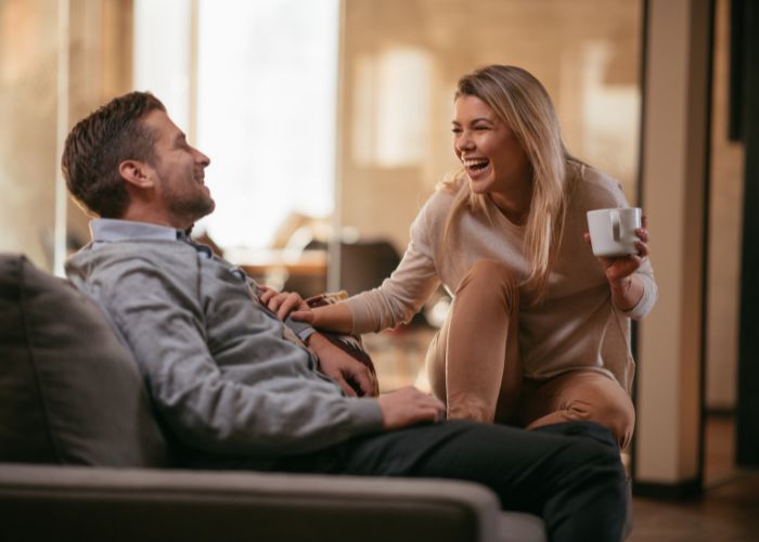 Laughing Couple Relaxes On A Sofa At Home While Sharing A Warm, Playful Conversation.