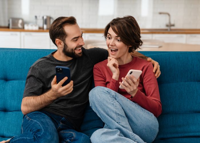 Couple Using Phone At Home On Sofa