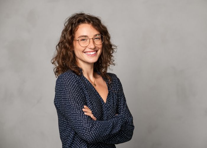 Smiling Woman With Glasses Standing Against A Gray Background