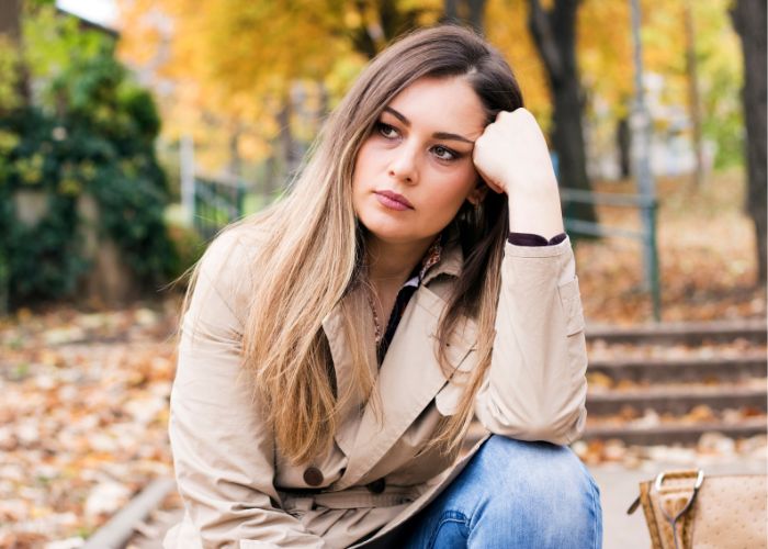 Young Woman Sitting Alone Outdoors With A Worried Expression, Reflecting On Relationship Problems.