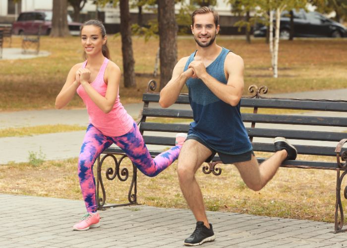 Couple Exercising Together Outdoors With Lunges Near A Park Bench.