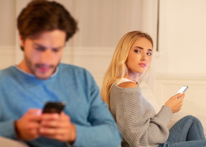 Girl Looking At Boyfriend Texting On Phone Suspecting Infidelity