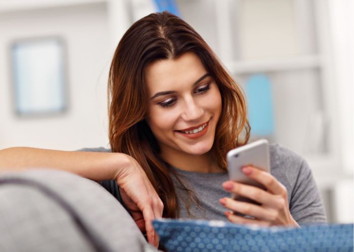 Woman Relaxing On A Sofa While Smiling At Her Smartphone.