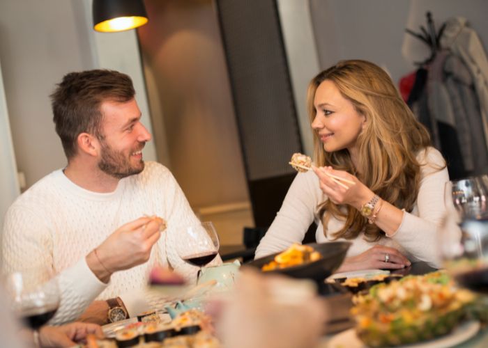 Couple Smiling Over Sushi And Wine During A Cozy Dinner At Home.