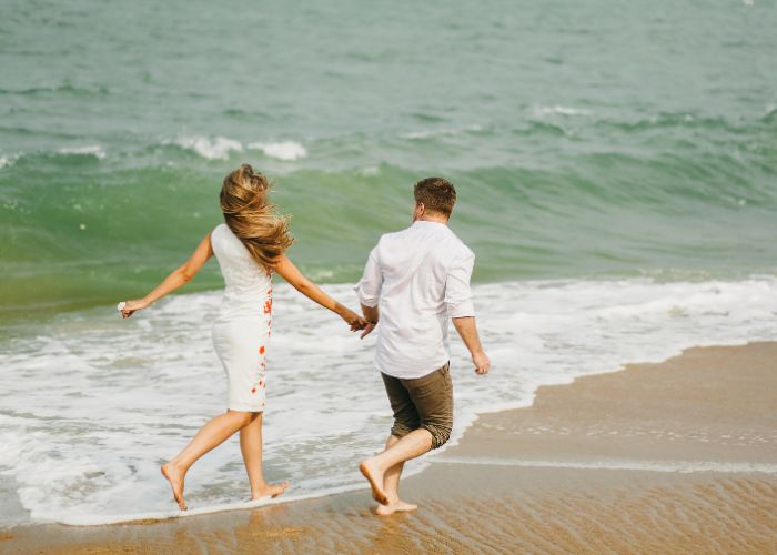 Couple Holding Hands And Running Along The Beach Shoreline During A Romantic Intentional Dating Experience